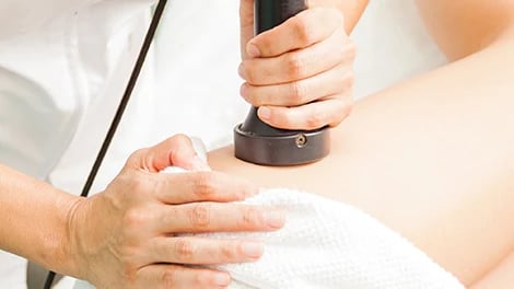 A hand holds a round treatment head against skin beside a white towel.